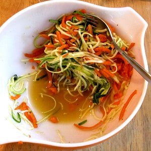 A bowl of spiralized zucchini and carrot, with liquid collecting in the bottom