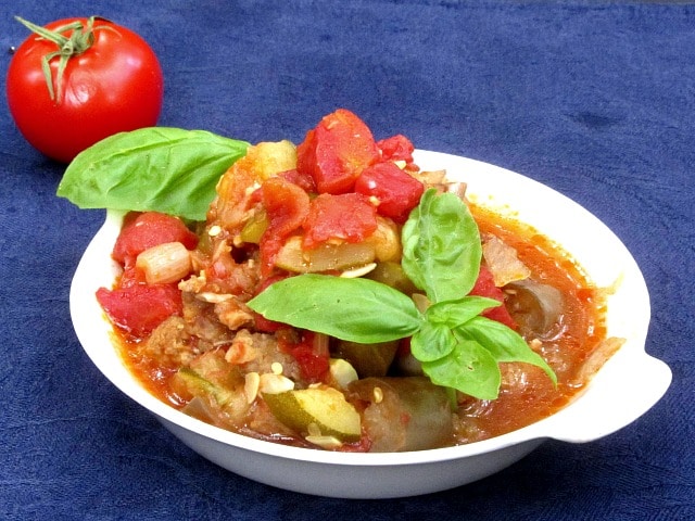 A dish of ratatouille with Italian sausage, garnished with basil